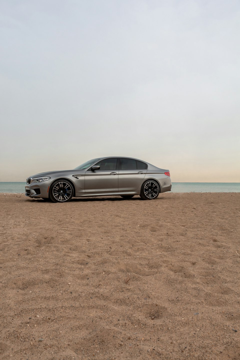 A silver sedan parked on the sand near the ocean.