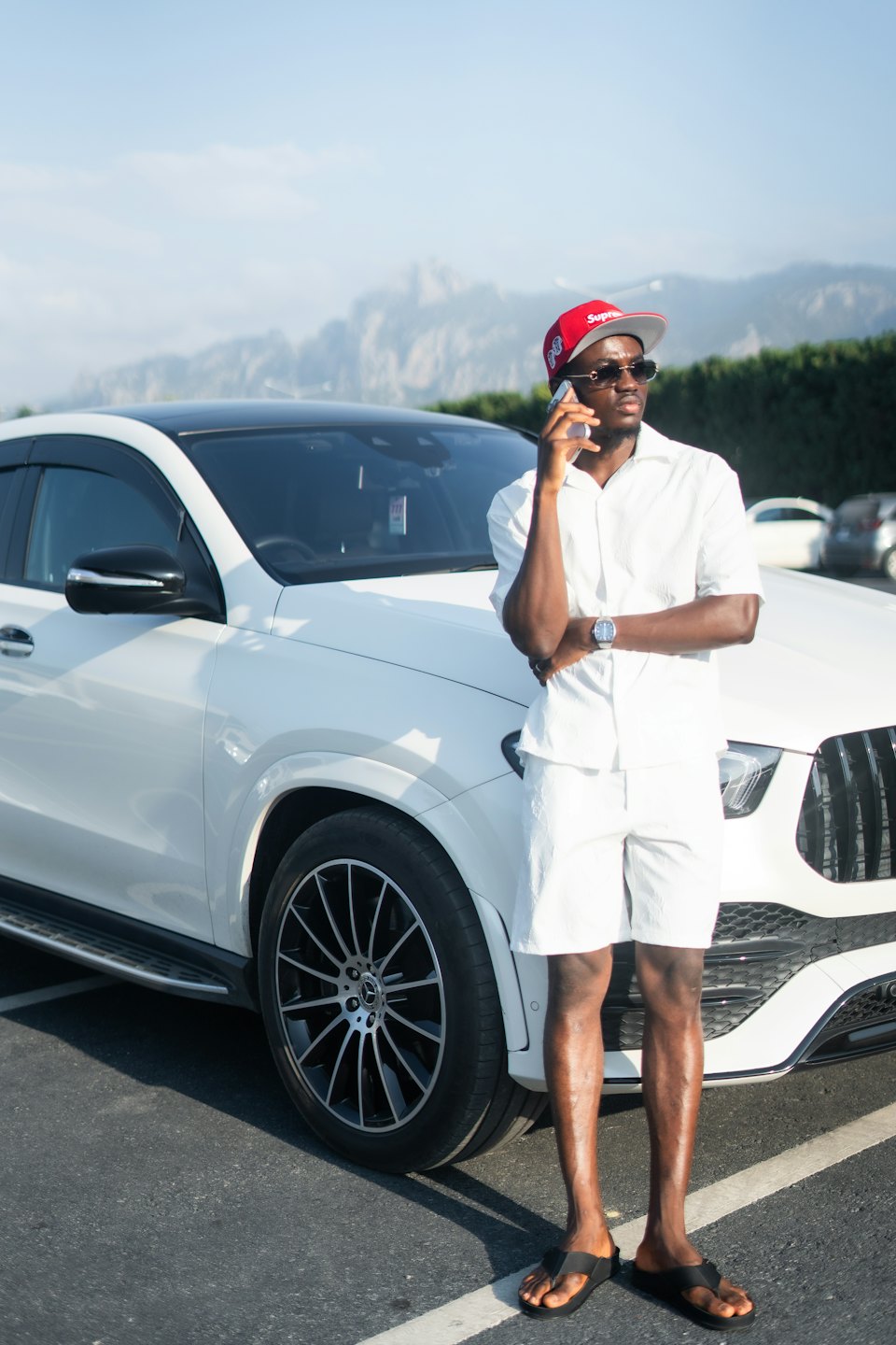 Man in a red cap talks on his phone beside a luxury SUV.